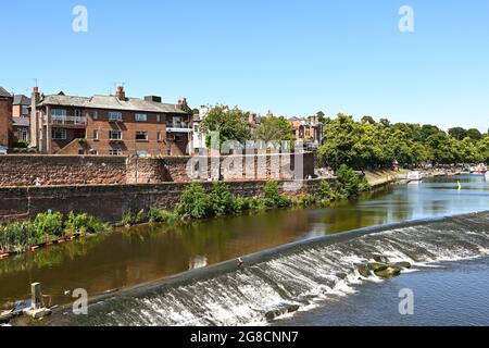 Chester, England - July 2021: Weir on the River Dee, which flows through the city. On the left is part of the city's wall. Stock Photo
