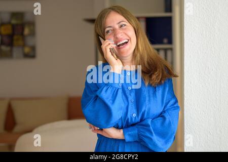 Stylish businesswoman chatting on her smartphone looking aside with a beaming smile and happy expression in a close up portrait Stock Photo