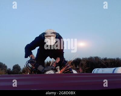 A man on the roof of a house works as a grinder. Stock Photo