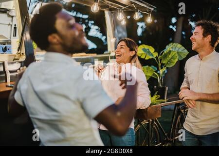 Diverse friends laughing outside food truck in evening Stock Photo
