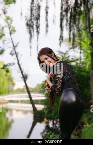 Pretty long-legged girl stands in a green park near water; she wears black  clothes (transparent top & shiny tight leggings) and golden sneakers Stock  Photo - Alamy