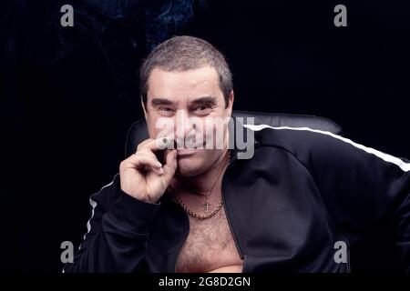 a funny and charming adult white man smokes a cigar and laughs and smiles looking at the camera. the grin of a Russian mafia bandit. Stock Photo