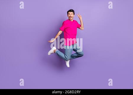 Full size photo of young happy cheerful excited smiling man jumping showing v-sign isolated on purple color background Stock Photo