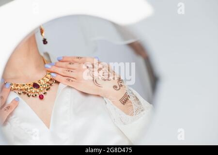reflection in mirror of young indian bride in earring wearing necklace on white Stock Photo