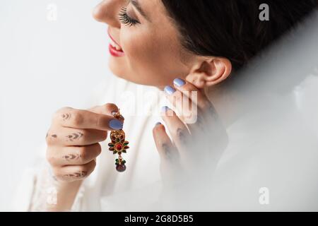 smiling indian bride wearing earring while getting ready for wedding isolated on white Stock Photo