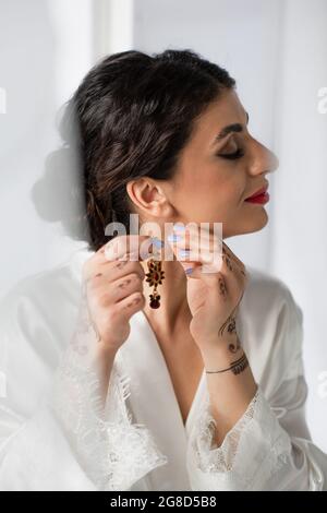 pretty indian bride wearing earring while getting ready for wedding on white Stock Photo