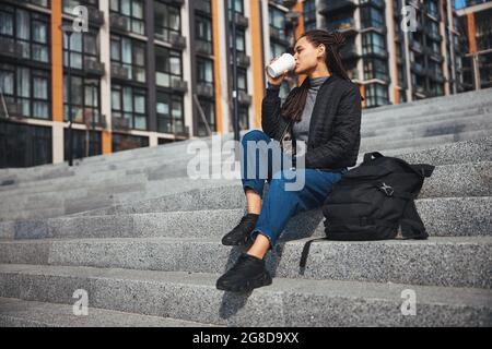 Thoughtful calm dark-haired pretty lady drinking coffee outdoors Stock Photo