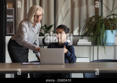 Elder coworker giving advice, explaining work process to Indian employee Stock Photo