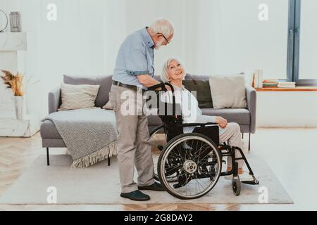 Disabled old man on wheel chair - Senior couple at home, partner coming back from hospital in convalescence Stock Photo