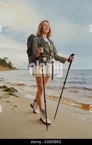 Optimistic traveller using walking poles during beach stroll Stock Photo