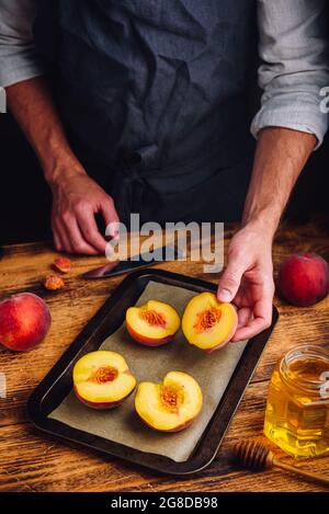 Roast halves of ripe peaches with honey. Chef puts fruits on baking dish Stock Photo
