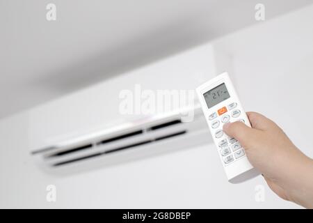Close up of a Female Hand operating a Remote control of a Domestic Air conditioner unit Stock Photo