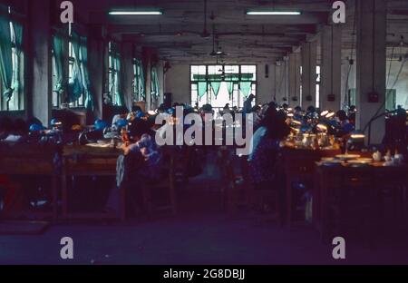 China 1983 a porcelain painting factory where exquisite designs are laboriously applied by women working under lights in a dimly lit room. Stock Photo