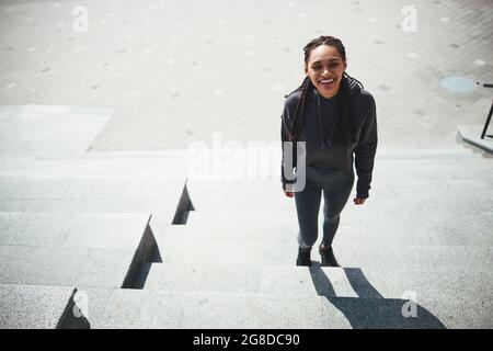 High-spirited woman with cornrows in activewear looking up Stock Photo