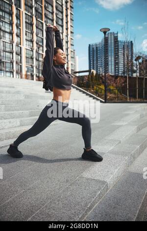 Smiling athletic female performing a stretching exercise outdoors Stock Photo