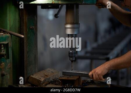 Close up of strong male hands using industrial drill press for making holes in metal construction. Craftsman processing steel at workshop. Manufacture concept. Stock Photo