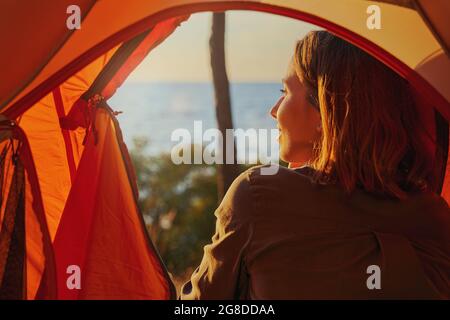 Person smiling joyfully at sunset from tent Stock Photo