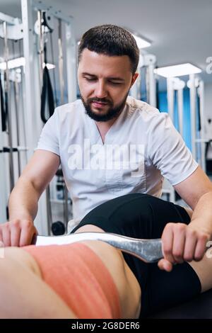 Young woman on massage bed on physio therapy. Chiropractic treatment of abs muscles using IASTM tool Stock Photo