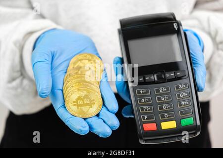 Bitcoin coins and pos terminal in woman hands in rubber gloves.  Stock Photo