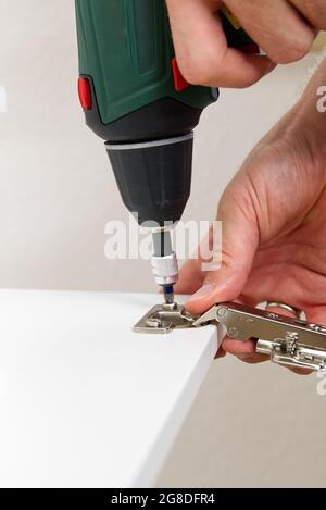 the carpenter screws the hinge on the furniture door. Furniture assembly service concept Stock Photo