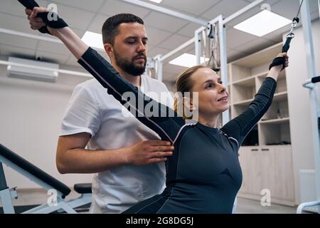 Physiotherapist treats hands of woman patient with stretching elastic band on rehabilitation trainer Stock Photo