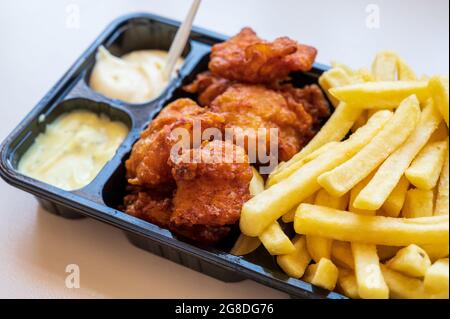 Dutch street food, portion of french fried potatoes, pieces of fried in oil cod fish fillet and two sauces close up Stock Photo