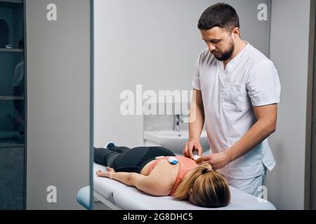 Doctor treats scoliosis in woman with electric stimulators. Myostimulation. Female patient