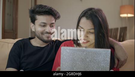 Young Indian couple spending time together while hugging and sitting on the sofa Stock Photo