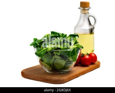 Mung bean salad leaves, corn salad in a glass bowl on a wooden board, cherry tomato, isolate. Fresh blend of green washed leaves and vegetable oil (Va Stock Photo