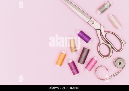 Tailor's work desk. Sewing accessories and fabric on a pink background. Sewing threads, needles, fabric, sewing centimeter or measuring tape. Top view Stock Photo