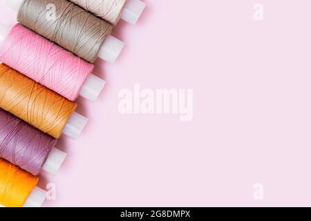 Tailor's work desk. Tailor or embroidery background. Pattern of color sewing threads or reels on pink background, top view copyspace. Colorful threads Stock Photo