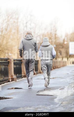 Full length back view at active senior couple running outdoors in winter