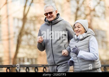 Waist up portrait of active senior couple running outdoors in winter and smiling happily, copy space Stock Photo