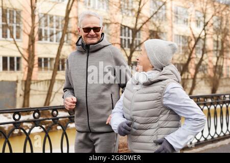 Waist up portrait of active senior couple jogging outdoors in winter and smiling happily, copy space