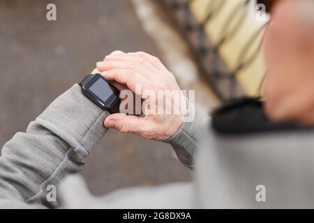 Close up of modern senior man checking smartwatch while running outdoors in winter, copy space Stock Photo