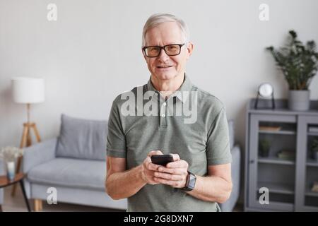 Minimal waist up portrait of smiling senior man using smartphone at home and looking at camera, copy space Stock Photo