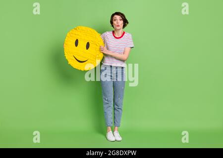 Full length body size view of pretty amazed girl holding in hands emoji sticker pout lips isolated over green pastel color background Stock Photo