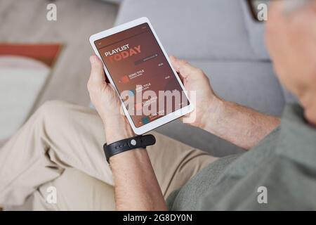 High angle closeup of modern senior man using digital tablet with playlist while listening to music at home, copy space Stock Photo