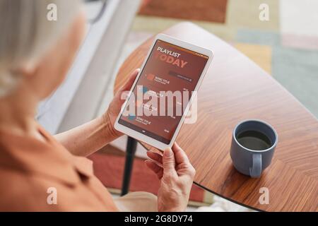 High angle closeup of modern senior woman using digital tablet with playlist while listening to music at home, copy space Stock Photo