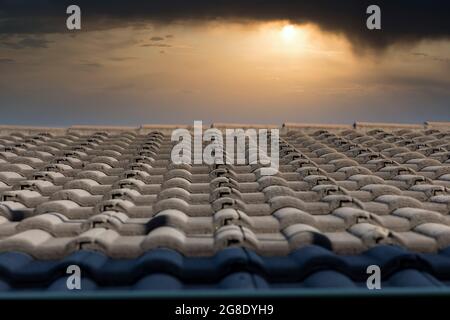 Grey terracotta roof tiles in a line on a roof in front of a sunset sky background Stock Photo