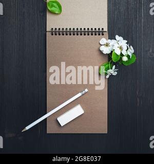 Blank kraft notepad, pencil, eraser and spring flowers on wood table background. Top view. Flat lay. Stock Photo