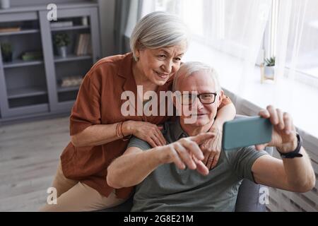 High angle portrait of happy senior couple using smartphone together at home and embracing Stock Photo