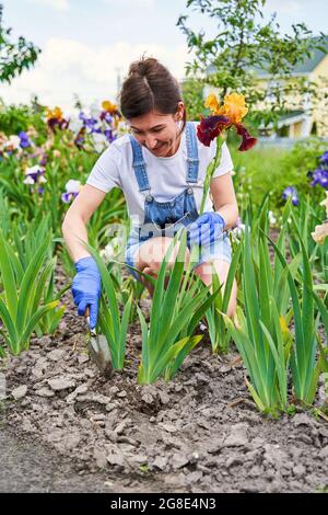 Housewife in blue gloves taking care of flower-garden Stock Photo