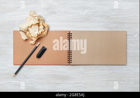 Photo of open blank kraft notebook, pencil, eraser and crumpled paper on light wood table background. Responsive design template. Flat lay. Stock Photo