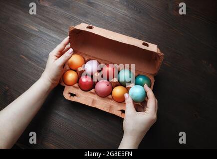 Colored Easter eggs in package and female hands on wood table background. Stock Photo