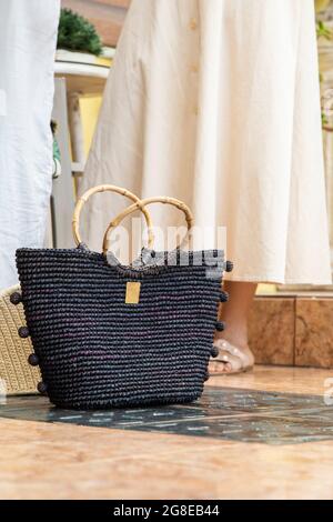 elegant black purse, woven, handmade accessory on the floor behind some people's legs, fashionable object in studio Stock Photo