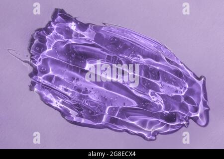 Hyaluronic acid texture, cosmetic product closeup with tiny bubbles. Glycerin or gel smear smudge swatch on lilac backdrop with shadow. Styling gel Stock Photo