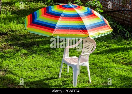 A colored parasol and a white plastic chair in the backyard of a private house. Stock Photo