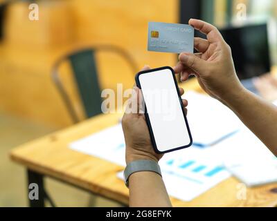 Male hands hold mobile phone and credit card, online transfer money, online purchasing, phone in blank screen Stock Photo