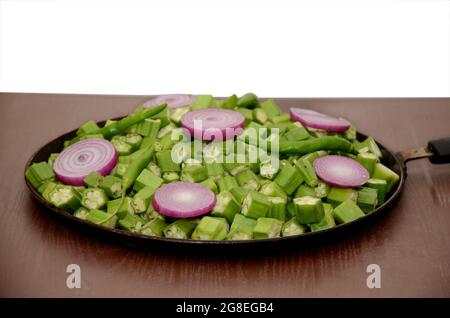 closeup the bunch ripe green sliced ladyfinger,onion,ripe green chilly in the fry pan isolated on white brown background. Stock Photo